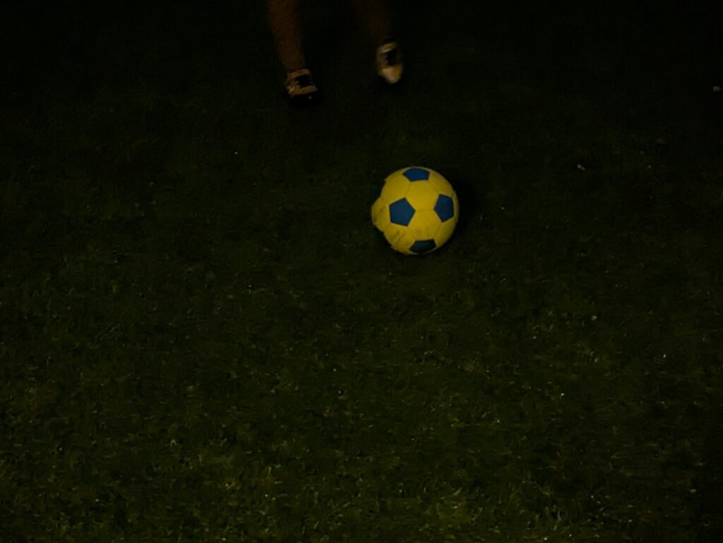 夜の庭でサッカーボールを蹴る6歳児